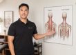 Dave Tam, RMT 主任 (Artemis 列治文健康诊所), 在斜方肌解剖图前讲解肩部解剖