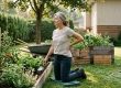 Gardener kneeling on a pad in a Richmond BC backyard garden, pausing with a hand on her lower back — gardening back pain recovery, Artemis Wellness Clinic