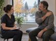 A practitioner takes notes during an initial assessment while a patient seated on a treatment table describes where his shoulder aches.